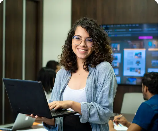 Moça sorrindo para a camera, segurando um notebook